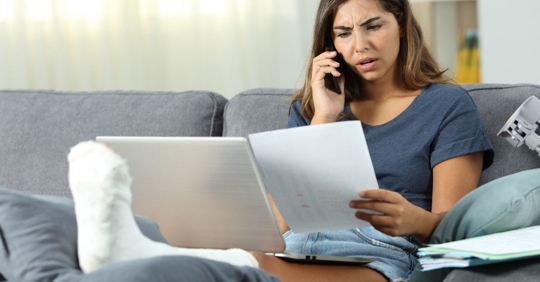 Woman with her leg in a cast talking on the phone holding papers in her hand.